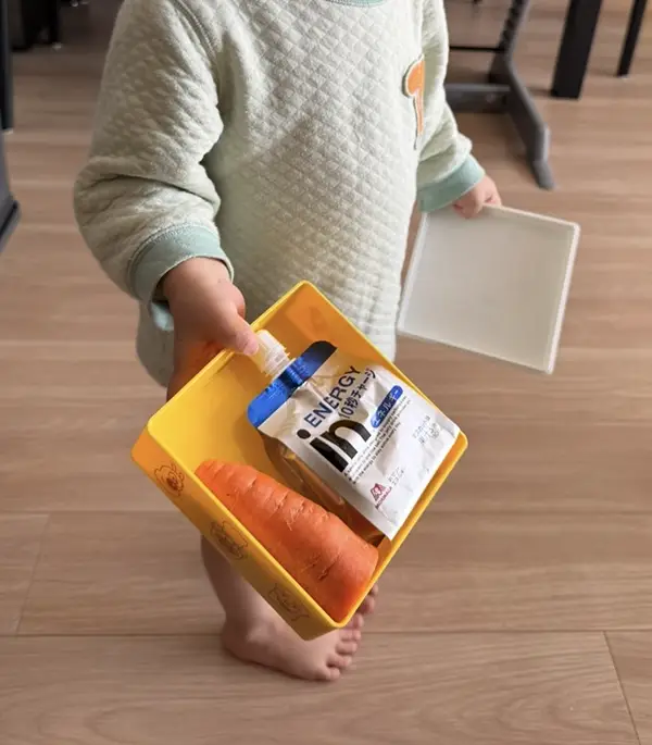 お弁当箱を差し出す2歳児の写真