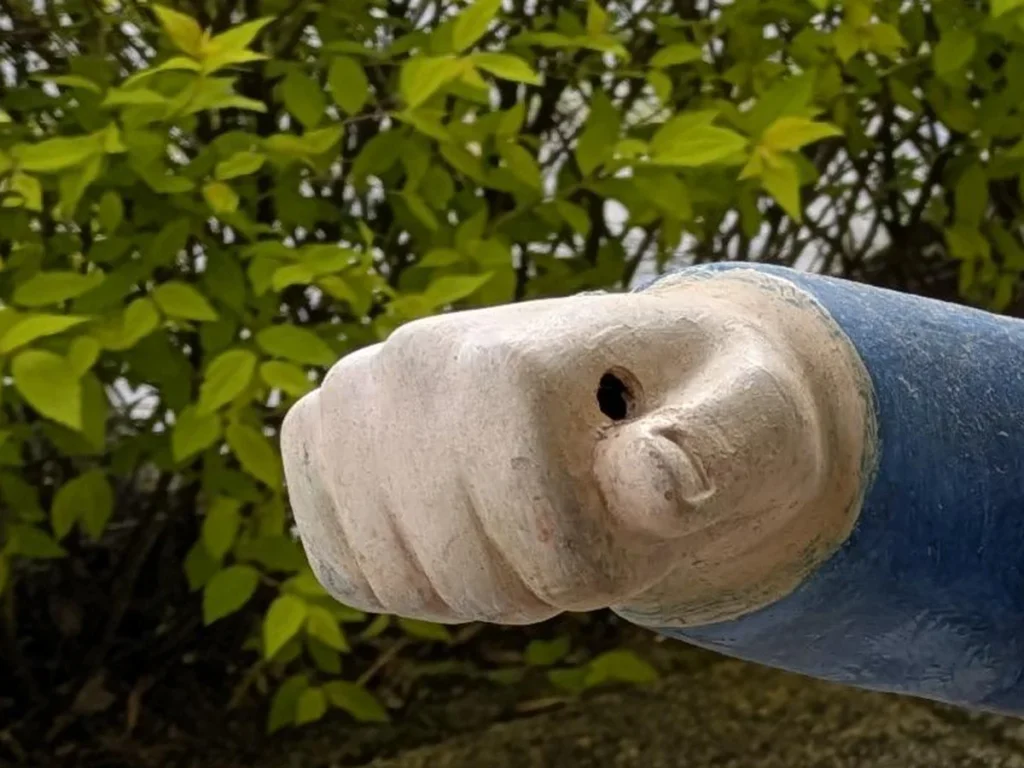 片手を前に突き出した、庭に置かれた小人の置物の写真